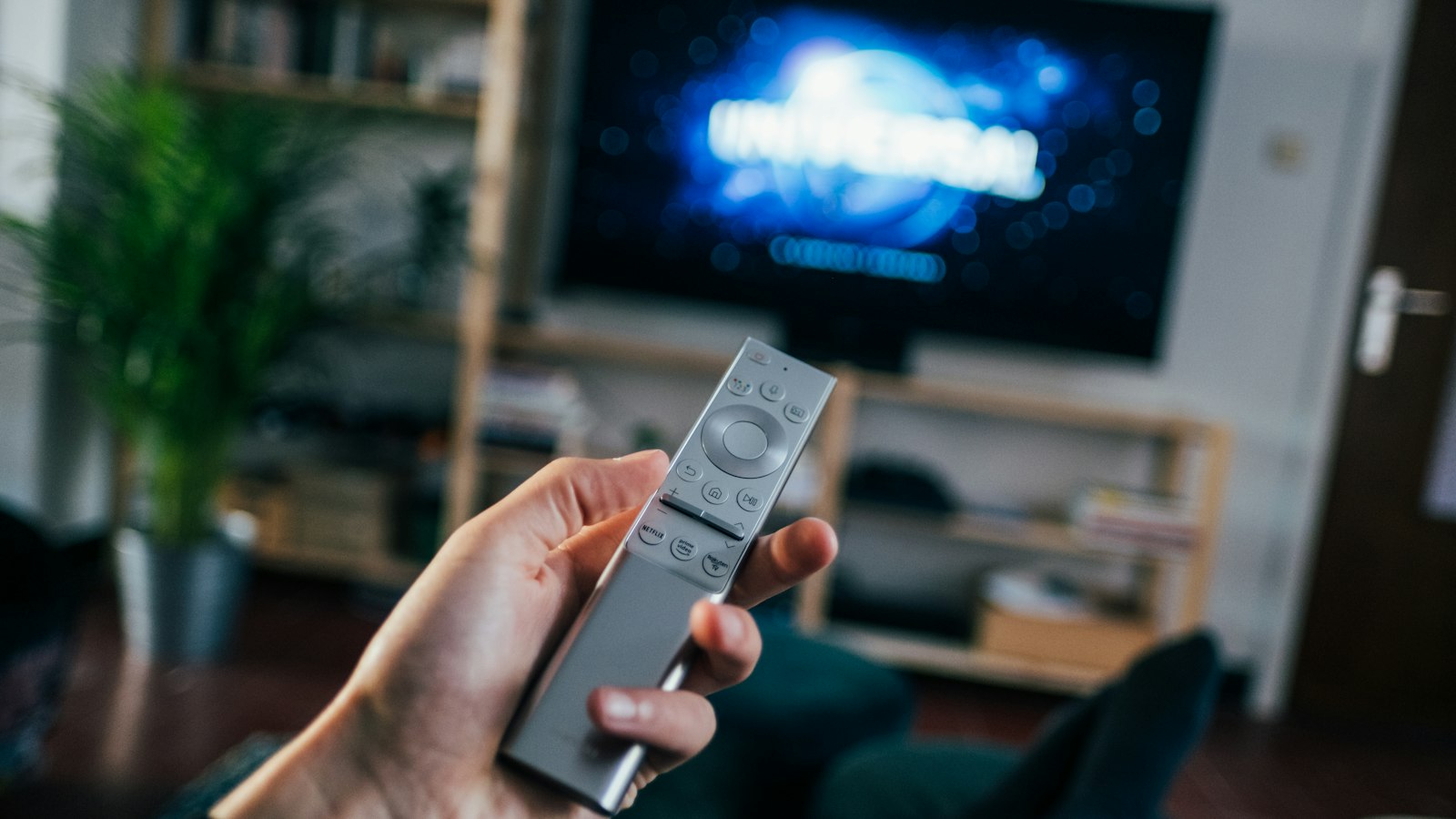Hand met afstandsbediening voor een tv in een woonkamer